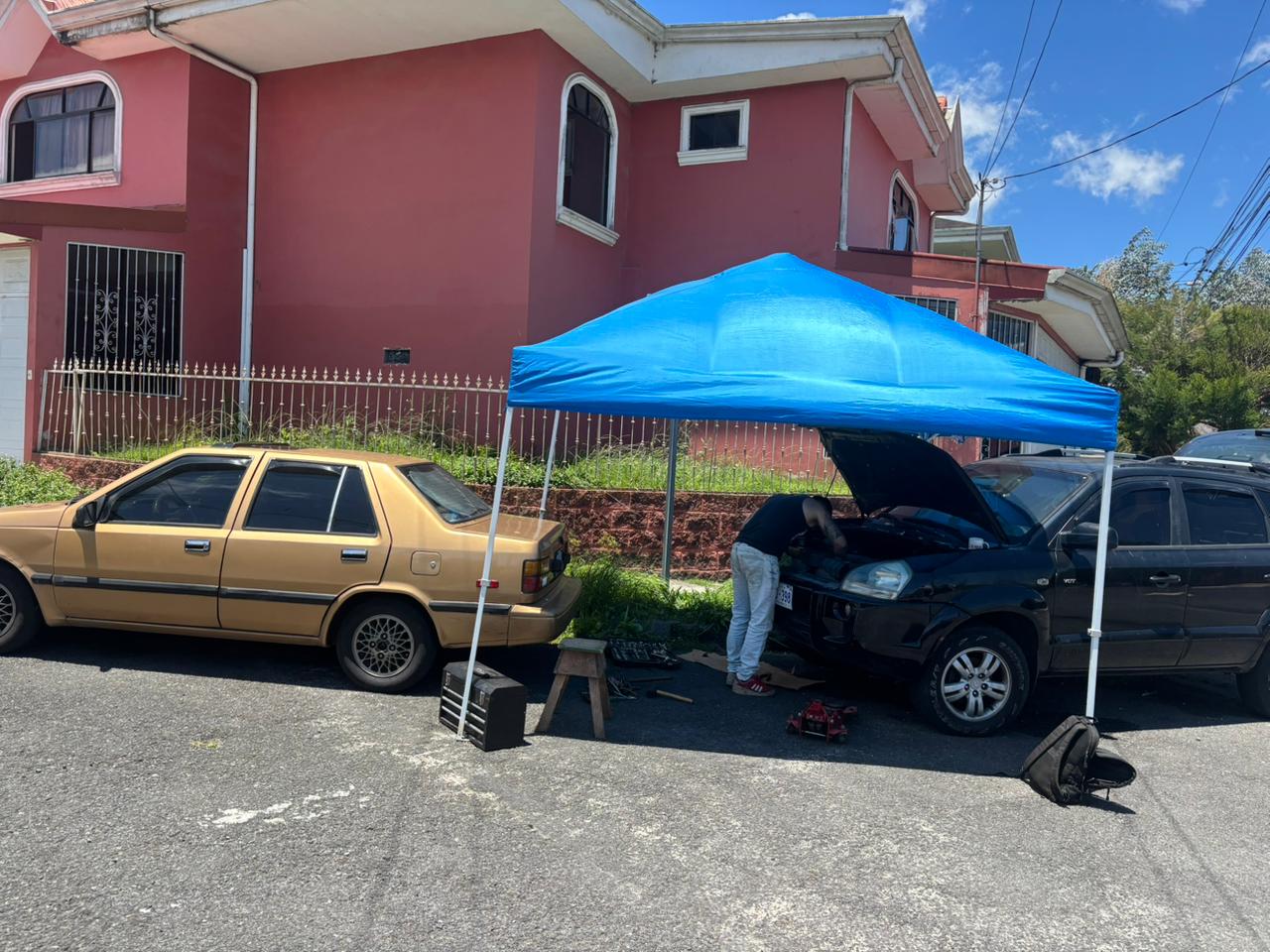 Reparación de una camioneta en la calle frente a una casa, bajo un toldo azul