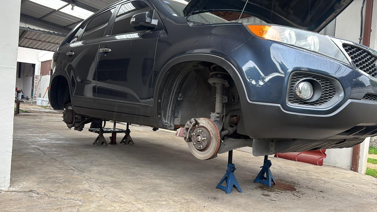 Kia Sorento levantado en torres dentro del taller, con la rueda delantera desmontada para revisar frenos